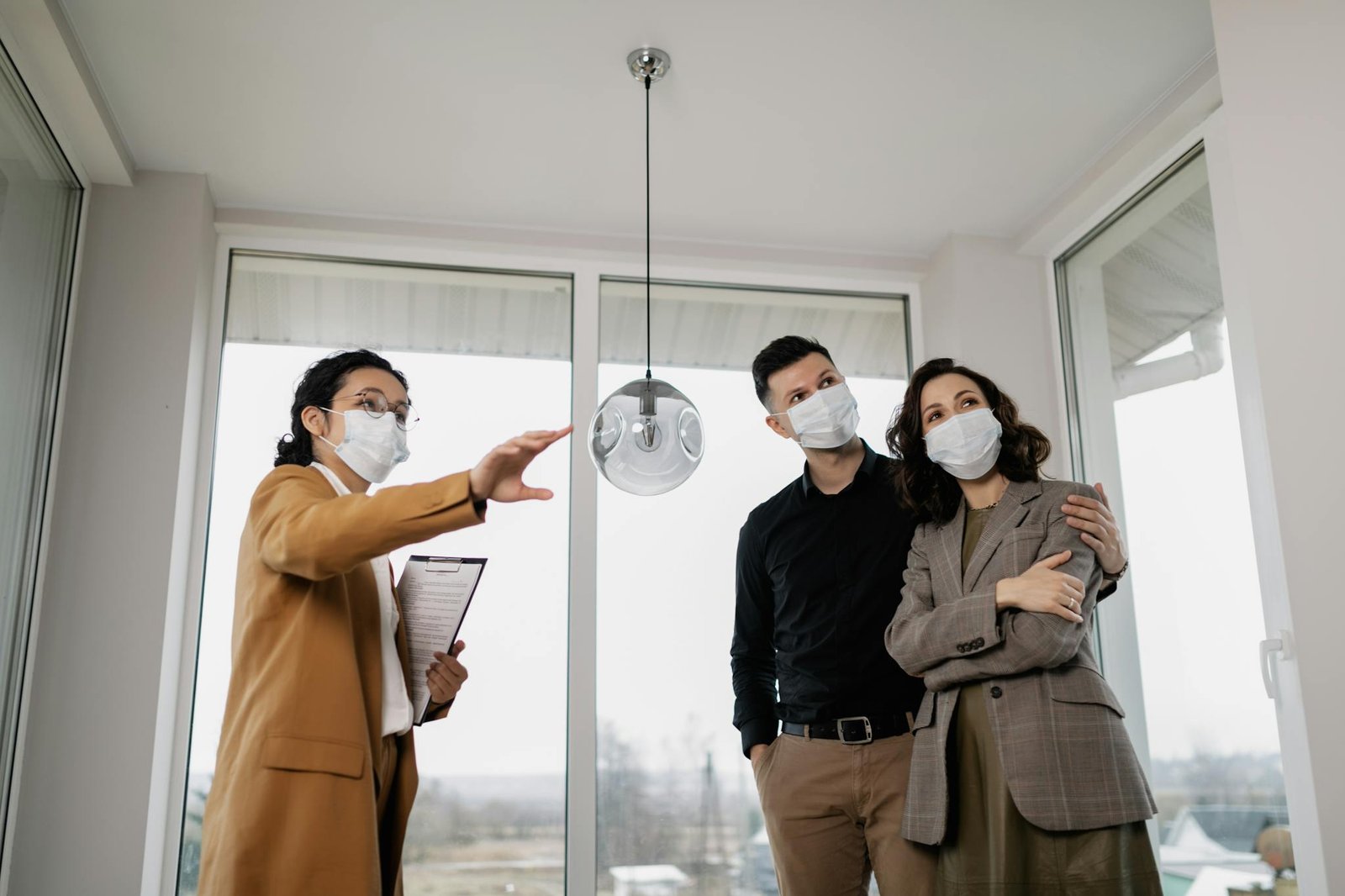 A realtor shows a masked couple a house interior, emphasizing safety during pandemic.